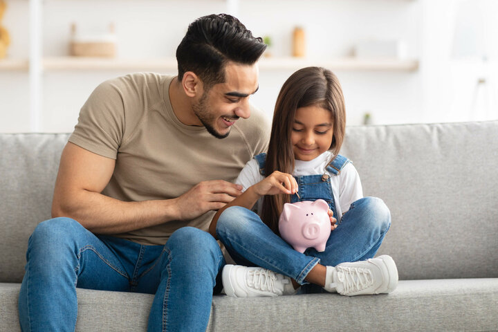 Kleines Mädchen wirft mit ihrem Vater Geld in ihr rosarotes Sparschwein